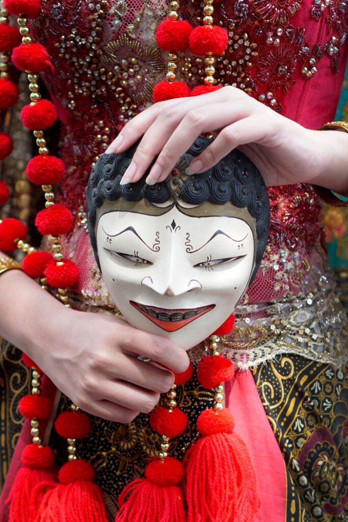 Intricate Indonesian mask held by hands, adorned with traditional beads and fabric.