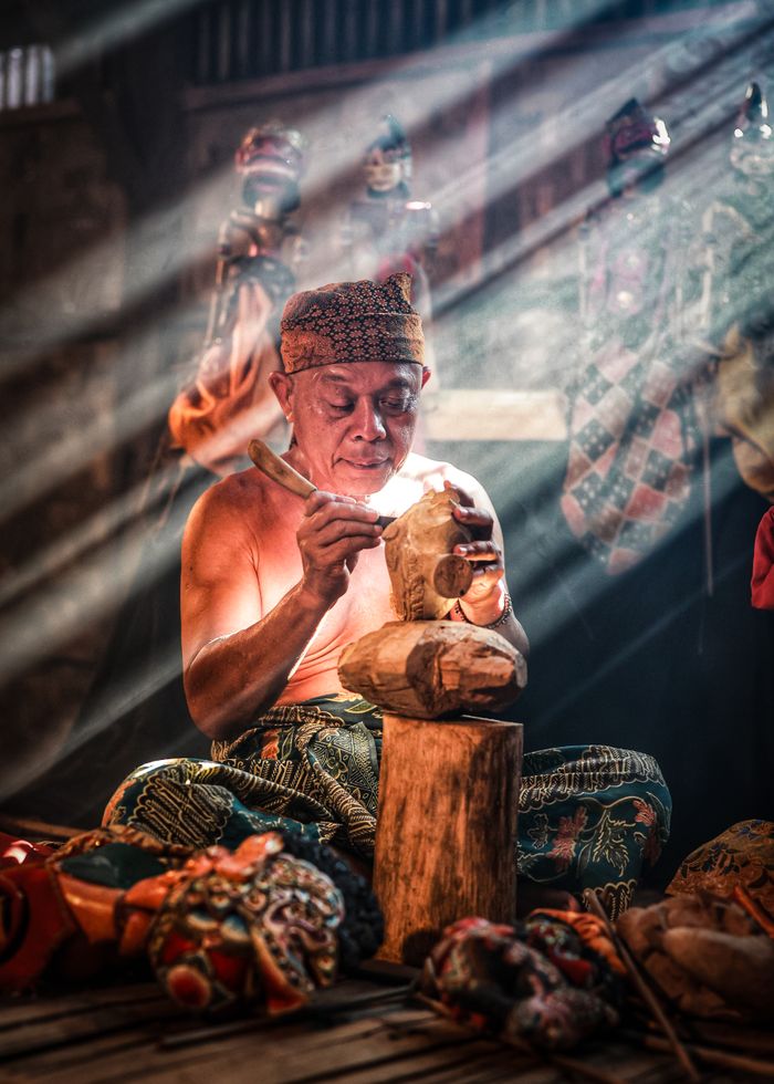 A skilled artisan in West Java intricately carves a traditional Javanese wooden puppet.
