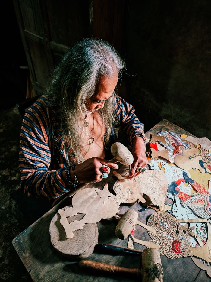 An artisan meticulously crafting traditional shadow puppets, showcasing detailed craftsmanship indoors.