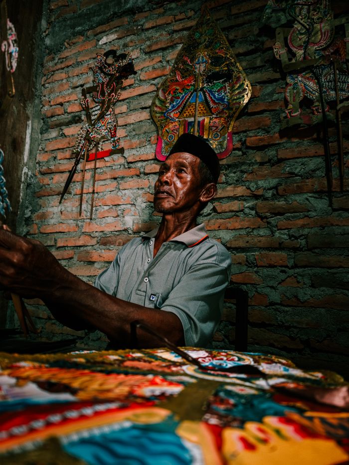 Traditional Indonesian artisan crafting wayang kulit shadow puppets with detailed cultural patterns.