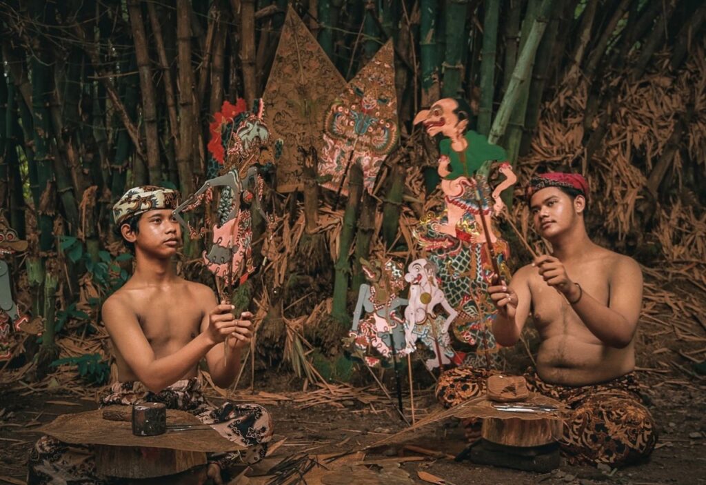Two performers engaged in a traditional Indonesian Wayang Kulit puppet show outdoors.